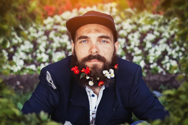 Sans-abri barbu assis dans un lit de fleurs — Photo