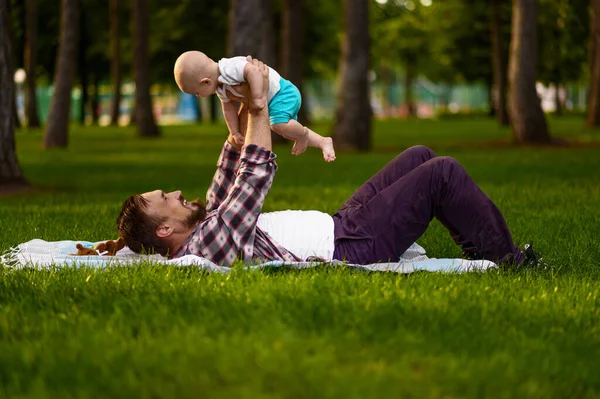 Padre y su pequeño bebé tumbados en el césped en el parque —  Fotos de Stock