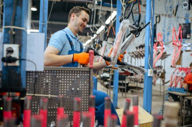 Bisiklet fabrikası, pembe çocuk bisikleti tutan işçiler. Üniformalı erkek tamirci bisiklet parçaları, atölyede montaj hattı, endüstriyel üretim
