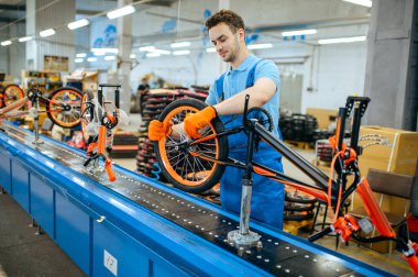Bisiklet fabrikası, montaj hattı işçisi, tekerlek montajı. Üniformalı erkek tamirci atölyeye bisiklet parçaları ve endüstriyel üretim kuruyor.