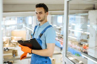 Bisiklet fabrikası, not defteri olan genç işçi bisiklet montaj hattında poz veriyor. Üniformalı erkek tamirci atölyeye bisiklet parçaları ve endüstriyel üretim kuruyor.