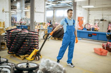 Bisiklet fabrikası, bisiklet tekerlekleri olan bir araba taşıyan işçiler. Üniformalı erkek tamirci bisiklet parçaları, atölyede montaj hattı, endüstriyel üretim