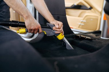 İşçi arabanın içini elektrikli süpürge, kuru temizleme ve temizlik ile temizliyor. Araç garajda yıkanıyor.