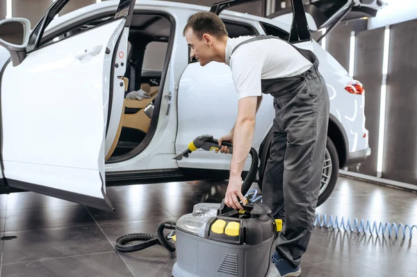 Worker removes dirt with vacuum cleaner, car dry cleaning and detailing. Vehicle washing service in garage, thoroughly care of automobile