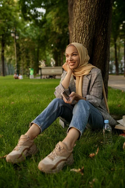 夏の公園でヒジャーブの笑顔のアラブの女の子 イスラム教徒の女性は芝生の上で休んでいる 宗教と教育 — ストック写真