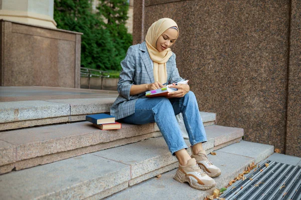 アラブ女子学生は大学の階段に座っている イスラム教徒の女性は ビジネスセンターの入り口に化粧を適用します 宗教と教育 — ストック写真