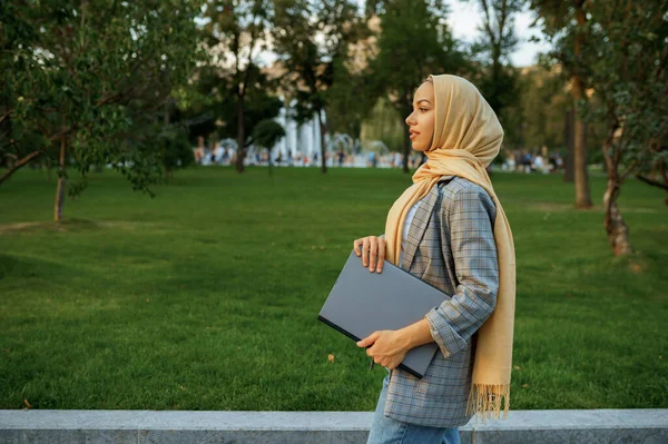 夏の公園をノートパソコンで歩くアラブの女性学生 イスラム教徒の女性は歩く道に休んでいる 宗教と教育 — ストック写真