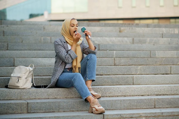 アラブ女性の学生がダウンタウンの階段に座っている イスラム教徒の女性は ビジネスセンターの入り口に化粧を適用します 宗教と教育 — ストック写真