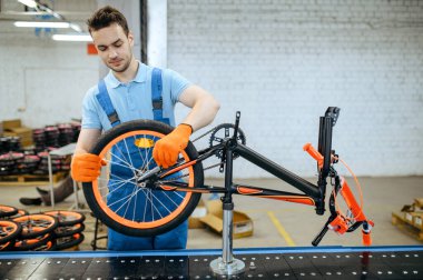 Bisiklet fabrikası, montaj hattı işçisi, tekerlek montajı. Üniformalı erkek tamirci atölyeye bisiklet parçaları yerleştirir