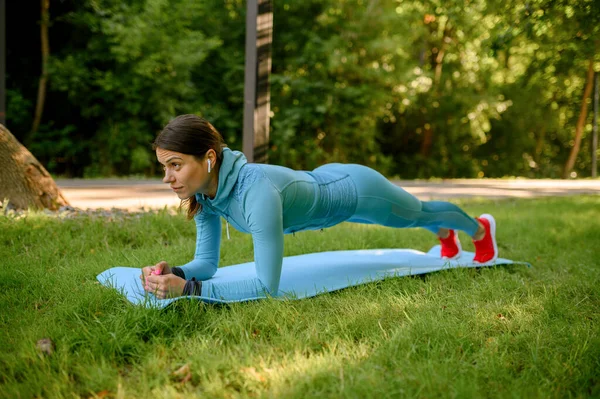 公園のマットで朝のフィットネストレーニング ヘッドフォンの女性 女性ランナーは 晴れた日にスポーツのために行きます 健康的なライフスタイル 屋外ワークアウトでジョギング — ストック写真