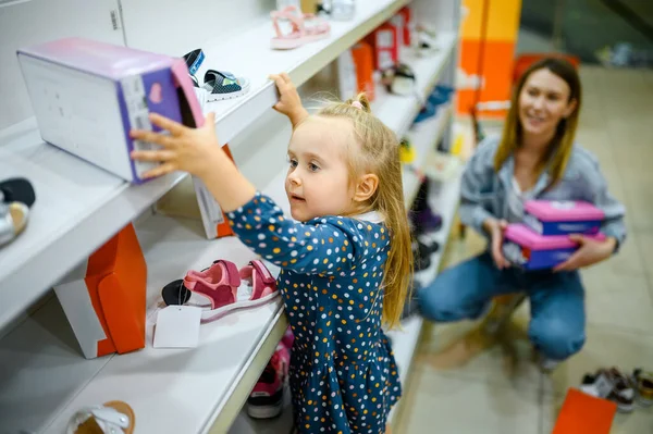 子供の店で靴を取るためにショーケースに小さな赤ちゃんが登ります 子供の店でサンダルを買うお母さんと愛らしい女の子 幸せな子供時代 家族は市場で購入する — ストック写真