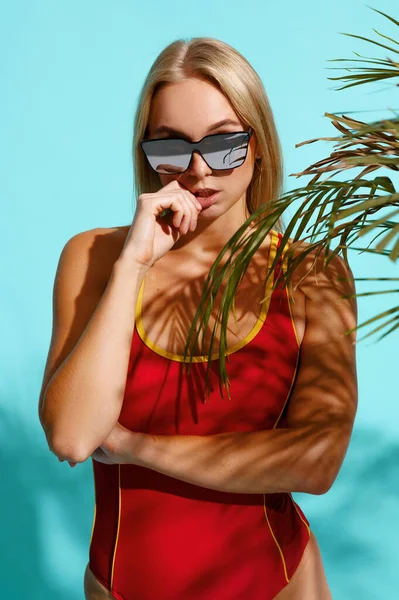 身穿红色泳衣的活泼女人在演播室里摆出青色的背景 穿着泳衣的女孩准备晒黑 穿着泳裤身材纤细的模特 迷人的女游泳选手 — 图库照片