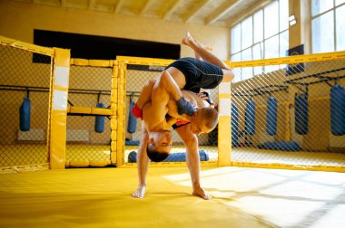Spor salonunda bir kafeste iki erkek dövüşçü dövüşüyor. Ringde kaslı adamlar, dövüş antrenmanı, dövüş sanatları eğitimi, yarışma ya da dövüş antrenmanı.