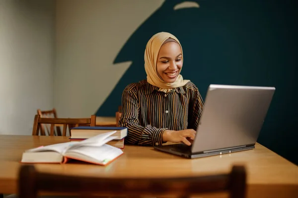 大学のカフェでラップトップを使用してヒジャーブのアラブ女性学生 図書館に座って本を持つイスラム教徒の女性 宗教と教育 — ストック写真