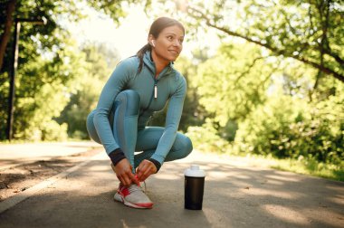 Parkta sabah antrenmanı, kulaklıklı gülümseyen bir kadın. Kadın koşucu güneşli bir günde spor için koşar, sağlıklı bir yaşam tarzı, açık havada spor eğitimi alan bir kız.