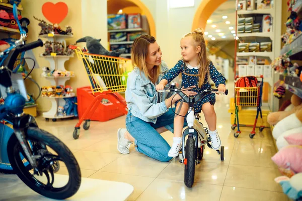 子供の店で自転車を買うママと可愛い女の子 ショーケースの近くの母と愛らしい娘 幸せな子供時代 家族は店で購入します — ストック写真