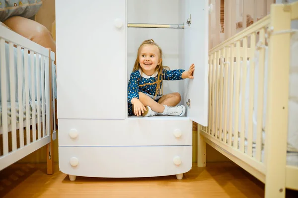 子供の店のベビーベッドの近くのワードローブに座って笑顔の女の子 Adorable Child Showcase Childrens Shop Happy Childhood Gaughter Makes — ストック写真