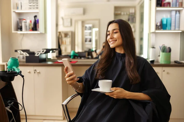 Cliente Femenino Sonriente Con Teléfono Taza Café Peluquería Mujer Sentada —  Fotos de Stock