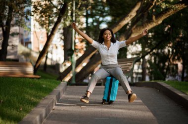 Yaz parkında bavulla gezen oyuncu bir kadın. Bagajı açık havada gezen bayan yolcu, çantalı yolcu doğada dinleniyor. Bagajı olan kız şehir sokağında rahatlar.