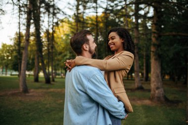 Parkta romantik bir yürüyüş yapan mutlu bir çift. Erkek ve kadın dışarıda, arka planda yeşil çimenler. Aile yazın çayırda dinlenir, haftasonu doğada.