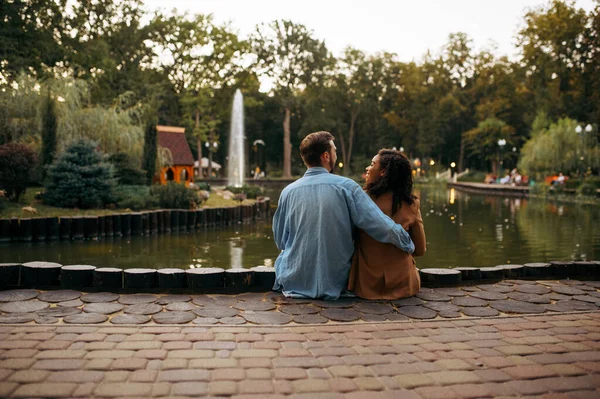 夏の公園で池を受け入れる愛のカップル 男と女は屋外でリラックスし 背景に緑の芝生 夏は湖の近く 週末は自然 — ストック写真