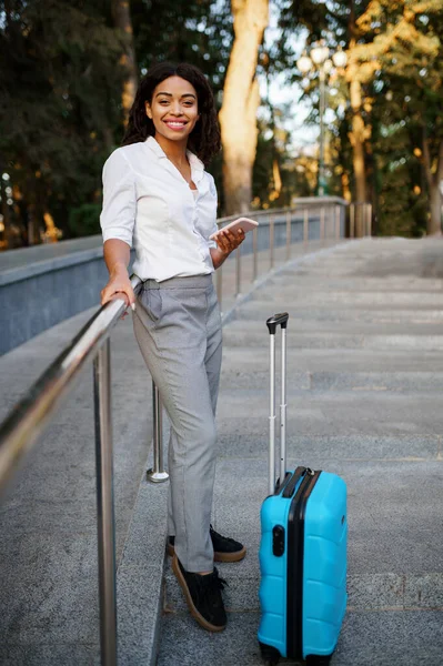 在夏季公园的楼梯上 身穿手提箱的微笑的女人摆出一副姿势 携带行李的女旅客在户外休息 携带行李的旅客在大自然中休息 带着行李的女孩在市区小巷里休息 — 图库照片