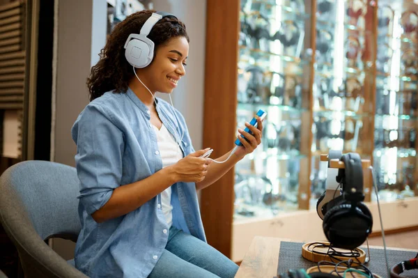 ヘッドフォン店で音楽を聴いている若い女性 オーディオショップの女性の人は 背景にイヤホンでショーケース マルチメディアサロンで買い手 — ストック写真