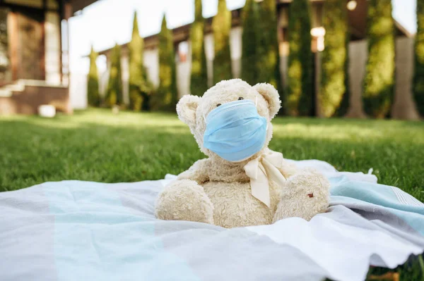 庭の毛布の上に座っているウイルス対策マスクにテディベア 裏庭の芝生の上のマスクで柔らかいおもちゃ 流行の危険性 危険な感染症 医療の概念 — ストック写真