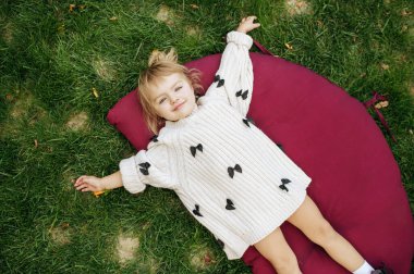 Bahçedeki çimlerin üzerinde yatan küçük kız. Kadın çocuk arka bahçedeki çimlerde poz veriyor. Çocuk dışarıda oyun oynuyor, mutlu bir çocukluk geçiriyor.