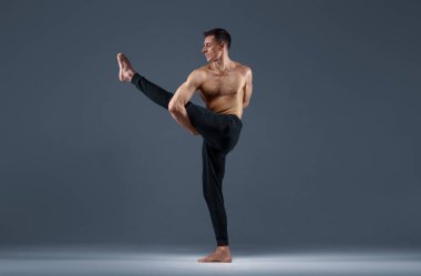 Erkek yogası stüdyoda esneme egzersizi yapıyor, gri arka plan. Yogi yapan güçlü bir adam, asana eğitimi, yüksek konsantrasyon, sağlıklı yaşam tarzı.