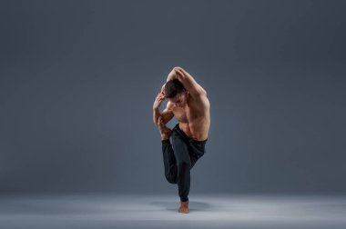 Yoga stüdyoda esneme egzersizi yapıyor, gri arka plan. Yogi yapan güçlü bir adam, asana eğitimi, yüksek konsantrasyon, sağlıklı yaşam tarzı.