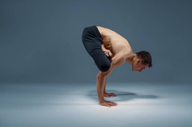 Kas yogası dengeyi zor bir pozisyonda tutar, meditasyon pozisyonu, gri arka plan. Yogi egzersizi yapan güçlü bir adam, asana eğitimi, yüksek konsantrasyon, sağlıklı yaşam tarzı.
