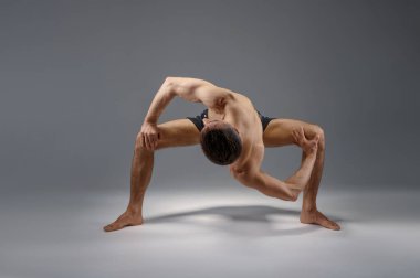 Erkek yoga zor bir pozisyonda duruyor, mükemmel esneme, meditasyon, gri arka plan. Yogi egzersizi yapan güçlü bir adam, asana eğitimi, yüksek konsantrasyon, sağlıklı yaşam tarzı.