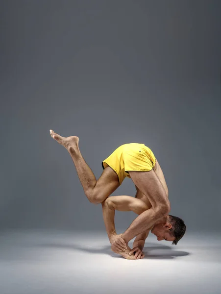 Male yoga in a difficult pose on hands, meditation, grey background. Strong man doing yogi exercise, asana training, top concentration, healthy lifestyle