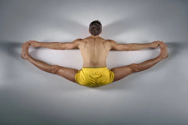 Male yoga sits on a twine, top view, grey background. Strong man doing yogi exercise, asana training, top concentration, healthy lifestyle