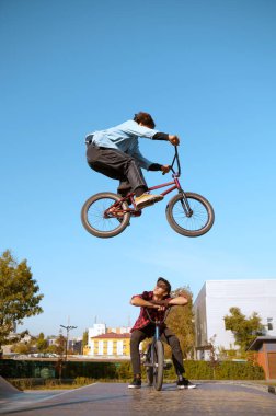 Bmx motorcusu rampada, hareket halinde atlıyor, paten alanında antrenman yapıyor. Aşırı bisiklet sporu, tehlikeli bisiklet egzersizi, sokak bisikleti, yaz parkında bisiklet süren gençler.