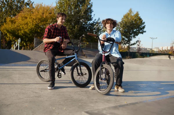 Two bmx bikers poses on ramp in skatepark. Extreme bicycle sport, dangerous cycle exercise, street riding, biking in summer park