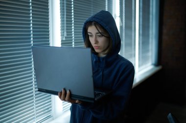 Kapüşonlu kadın internet korsanı laptopta çalışıyor.