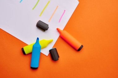 Kağıt yaprağın üzerinde inmelerle açılmış renkli keçeli kalemler. Ofis kırtasiye malzemeleri, okul veya eğitim aksesuarları, yazı ve çizim araçları