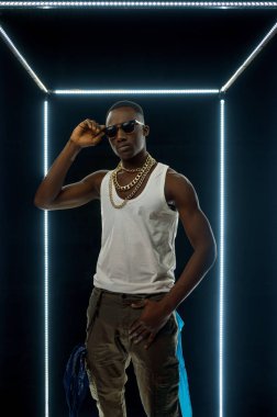 Altın mücevher giymiş rapçi aydınlatılmış küp pozları veriyor.