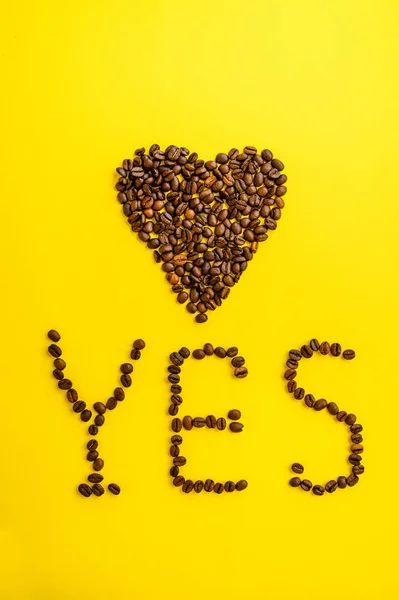 Coffee bean heart and yes word, yellow background — Stock Photo, Image