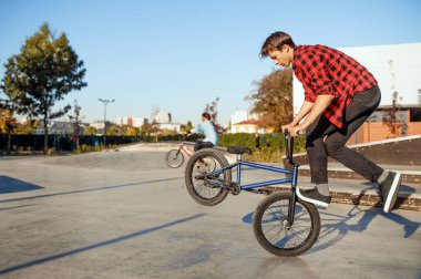 İki erkek BMX motorcusu kaykay parkında numaralar yapıyor.