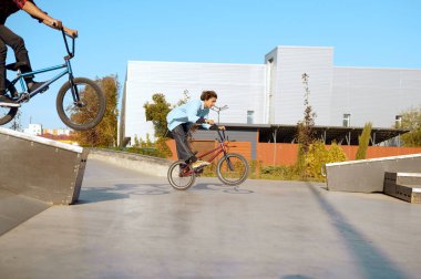İki erkek BMX motorcusu kaykay parkında numaralar yapıyor.