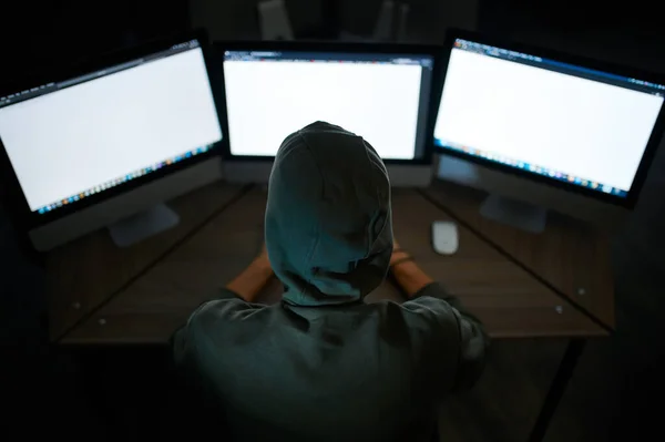 フードの男性のインターネットハッカーモニターに座って バックビュー 職場での違法Webプログラマー 犯罪者の職業 データハッキングサイバーセキュリティ — ストック写真
