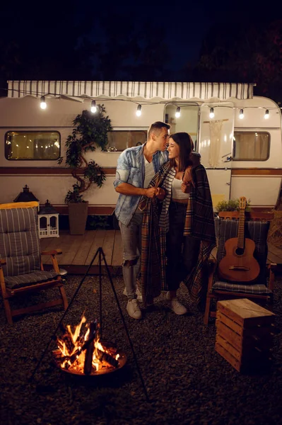 キャンプファイヤーでキスをする若い愛のカップル 森の中のキャンプでピクニック Rvの夏の冒険 キャンプカーを背景に たき火で男と女のレジャー トレーラーで旅行 — ストック写真