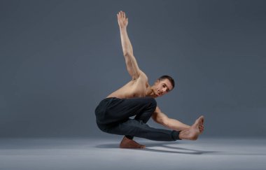 Yoga stüdyoda esneme egzersizi yapıyor, gri arka plan. Yogi yapan güçlü bir adam, asana eğitimi, yüksek konsantrasyon, sağlıklı yaşam tarzı.