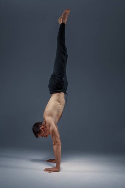 Erkek yogası dengeyi sağlıyor, meditasyon pozisyonu, gri arka plan. Yogi egzersizi yapan güçlü bir adam, asana eğitimi, yüksek konsantrasyon, sağlıklı yaşam tarzı.