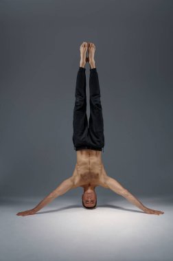 Kafasında ve ellerinde duran erkek yogası, meditasyon, gri arka plan. Yogi egzersizi yapan güçlü bir adam, asana eğitimi, yüksek konsantrasyon.