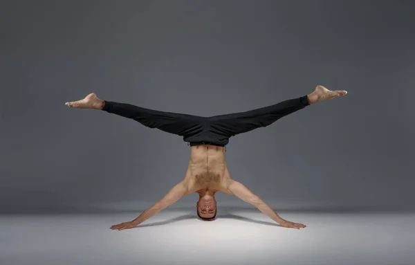 Male yoga standing on his head and hands, meditation, grey background. Strong man doing yogi exercise, asana training, top concentration