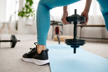 Dambılla egzersiz yapan bir kız, dizüstü bilgisayarda spor yapan bir kız. Spor giyim, internet sporları, arka planda oda içi.